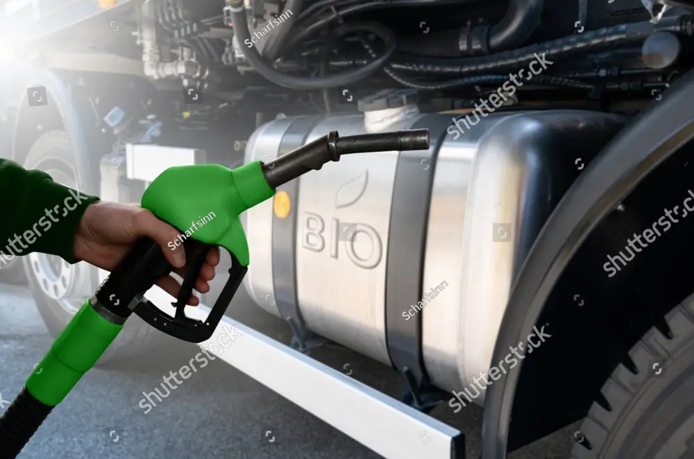 hand holding gree fuel pump nozzle with truck's bio fuel tank in the background